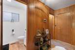 Step into a charming entryway featuring warm wood paneling and a convenient doorway leading to a bright, white bathroom.