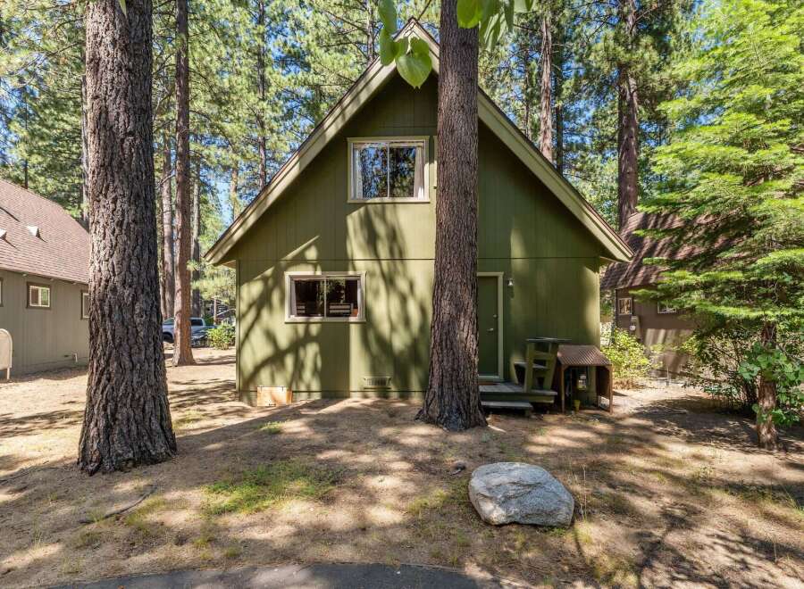 Nestled amongst tall pine trees, this charming green cabin offers a serene retreat.