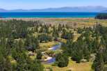 Discover this stunning property featuring a serene river winding through lush green trees and meadows, leading to a breathtaking view of a vast blue lake and distant mountains.
