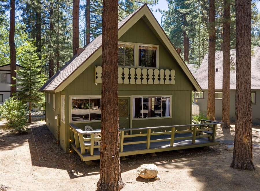 Nestled amongst tall pine trees, this charming green cabin offers a serene retreat.