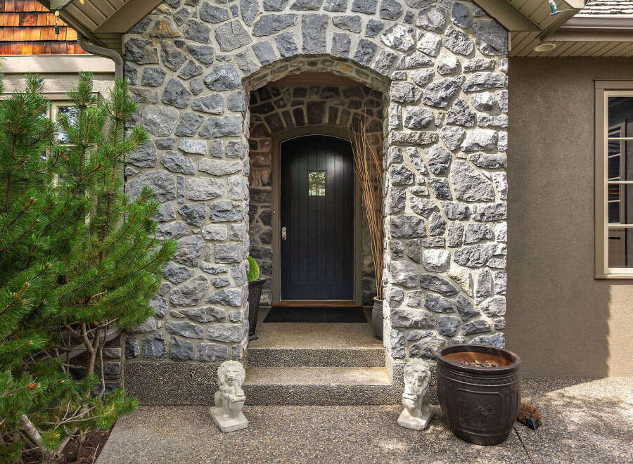 This charming home features a grand stone entryway with an arched doorway leading to a dark wooden door.