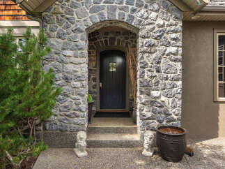 This charming home features a grand stone entryway with an arched doorway leading to a dark wooden door.
