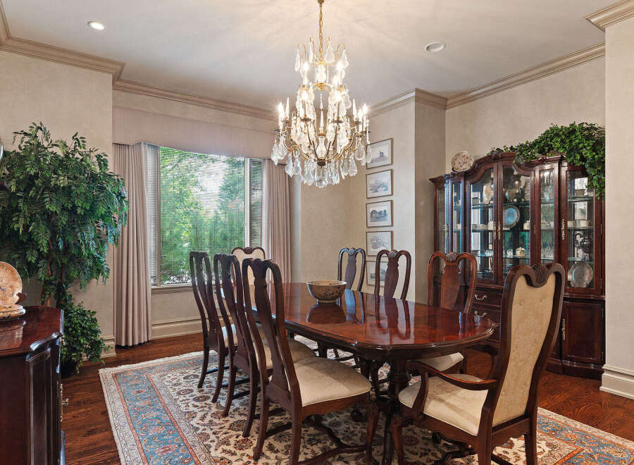 Elegantly set dining room featuring a large, polished mahogany table surrounded by ornate wooden chairs with upholstered seats.