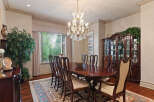 Elegantly set dining room featuring a large, polished mahogany table surrounded by ornate wooden chairs with upholstered seats.