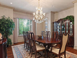 Elegantly set dining room featuring a large, polished mahogany table surrounded by ornate wooden chairs with upholstered seats.