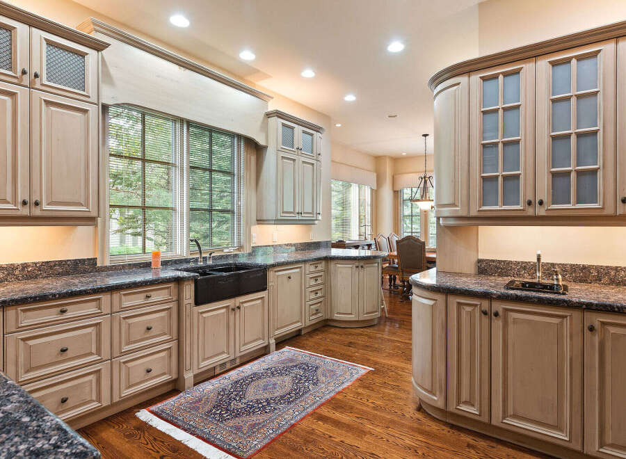 This spacious kitchen boasts custom light wood cabinetry with glass-front upper cabinets and intricate detailing.