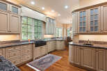 This spacious kitchen boasts custom light wood cabinetry with glass-front upper cabinets and intricate detailing.
