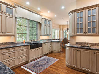 This spacious kitchen boasts custom light wood cabinetry with glass-front upper cabinets and intricate detailing.