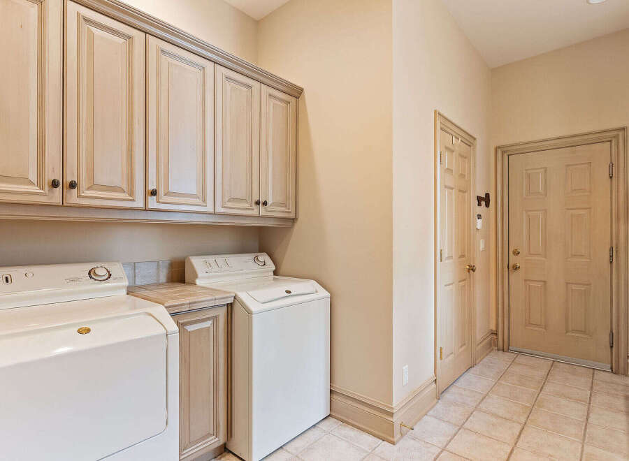 This laundry room offers ample storage with a full wall of light wood cabinets above the washer and dryer.