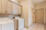 This laundry room offers ample storage with a full wall of light wood cabinets above the washer and dryer.
