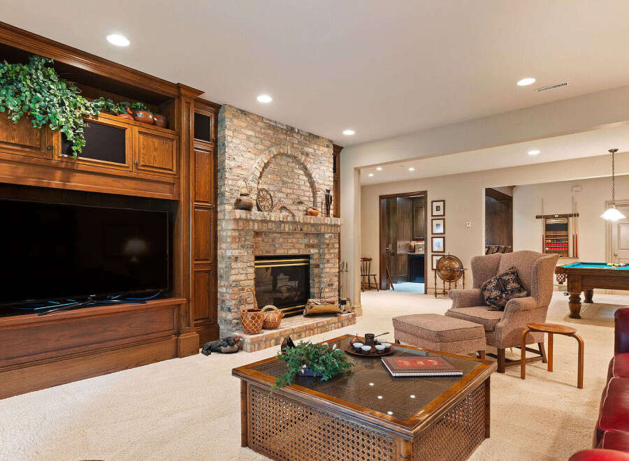 This luxurious basement living area features a stunning brick fireplace and a large built-in entertainment center, perfect for cozy evenings.