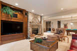 This luxurious basement living area features a stunning brick fireplace and a large built-in entertainment center, perfect for cozy evenings.
