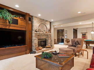 This luxurious basement living area features a stunning brick fireplace and a large built-in entertainment center, perfect for cozy evenings.