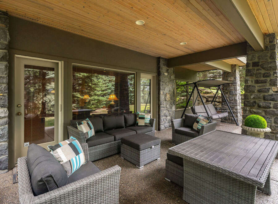 Enjoy outdoor living at its finest on this expansive covered patio, featuring a comfortable sectional sofa, a stylish coffee table, and a relaxing swing.