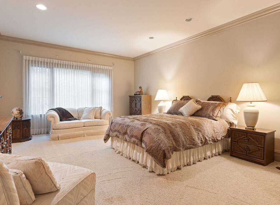 Experience luxurious comfort in this spacious master suite, featuring a plush king-sized bed adorned with elegant bedding and complemented by two charming nightstands with lamps.