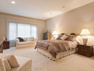 Experience luxurious comfort in this spacious master suite, featuring a plush king-sized bed adorned with elegant bedding and complemented by two charming nightstands with lamps.