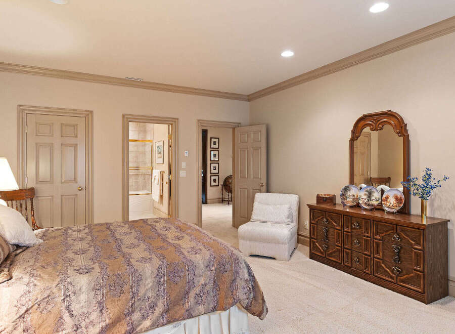 This spacious bedroom features a luxurious king-sized bed with an ornate comforter, complemented by a classic wooden dresser with a large mirror.