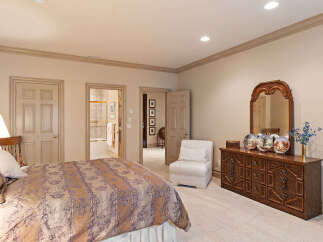 This spacious bedroom features a luxurious king-sized bed with an ornate comforter, complemented by a classic wooden dresser with a large mirror.