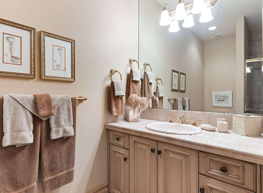 This elegant bathroom features a vanity with a tiled countertop and a large mirror, complemented by decorative framed artwork and plush towels.