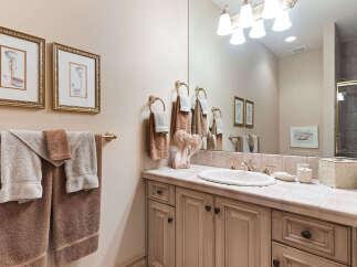 This elegant bathroom features a vanity with a tiled countertop and a large mirror, complemented by decorative framed artwork and plush towels.