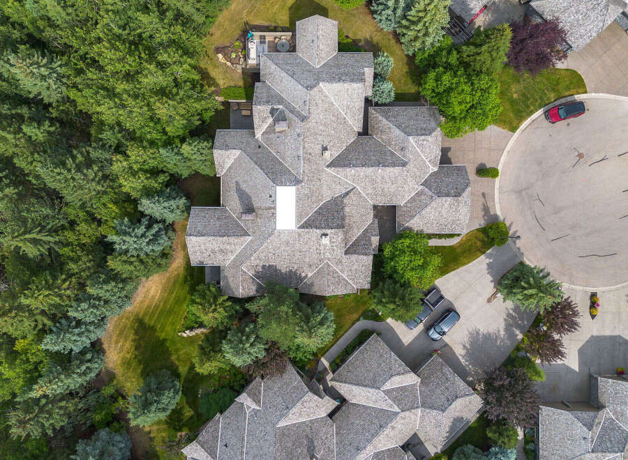 Experience luxury living in this stunning aerial view of a multi-level home featuring a complex, multi-faceted roofline and surrounded by lush greenery.