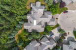 Experience luxury living in this stunning aerial view of a multi-level home featuring a complex, multi-faceted roofline and surrounded by lush greenery.