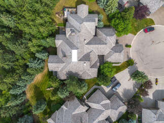 Experience luxury living in this stunning aerial view of a multi-level home featuring a complex, multi-faceted roofline and surrounded by lush greenery.