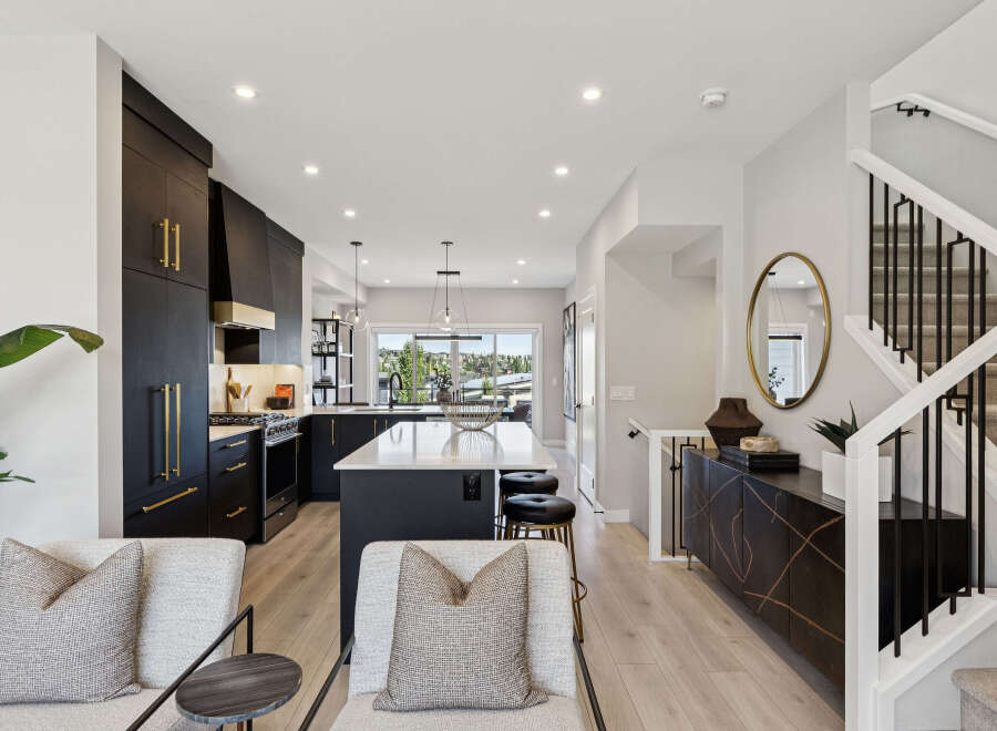 Experience modern luxury in this stunning kitchen and living area, featuring sleek dark cabinetry with elegant gold hardware and a spacious island perfect for entertaining.