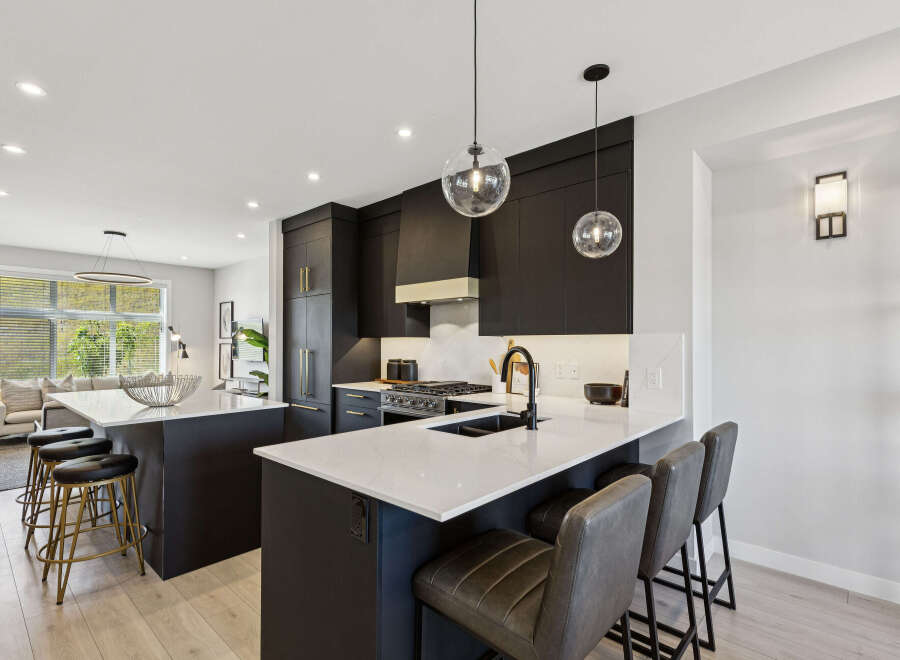 Experience modern luxury in this stunning kitchen, featuring sleek dark cabinetry, a spacious quartz island with seating, and a professional-grade gas range.