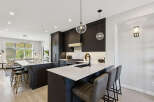Experience modern luxury in this stunning kitchen, featuring sleek dark cabinetry, a spacious quartz island with seating, and a professional-grade gas range.