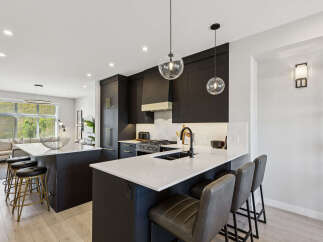 Experience modern luxury in this stunning kitchen, featuring sleek dark cabinetry, a spacious quartz island with seating, and a professional-grade gas range.