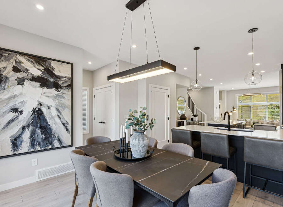 Experience modern living in this open-concept dining and kitchen area, featuring a sleek rectangular chandelier and a striking abstract artwork.