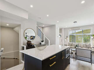 Experience modern living in this stunning open-concept home, featuring a sleek kitchen island with quartz countertops and gold accents.