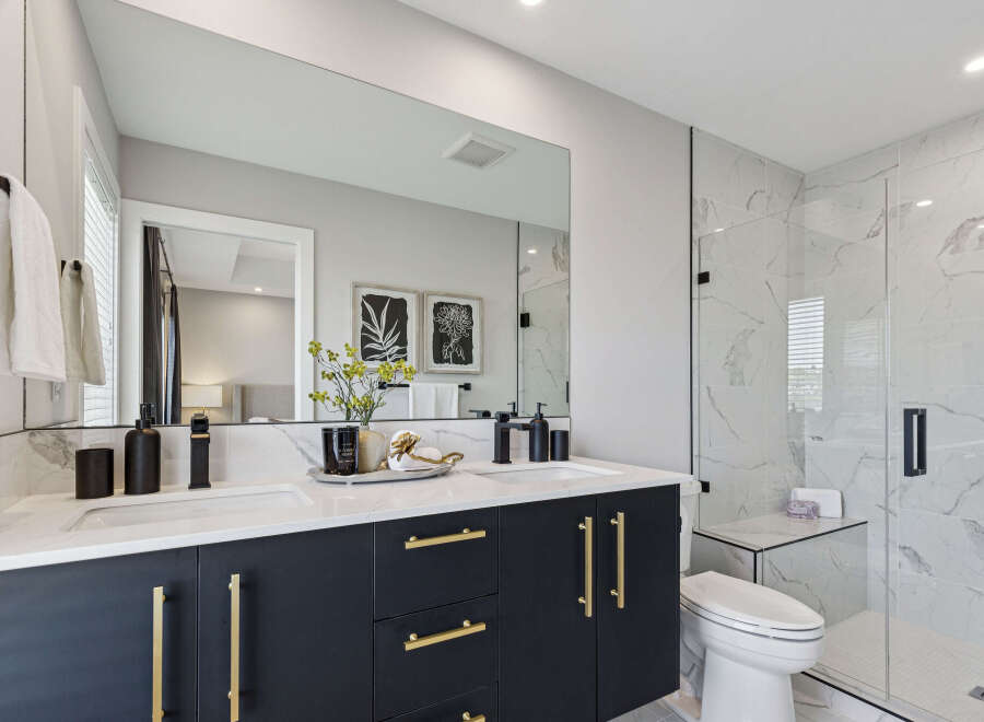 Experience modern luxury in this stunning bathroom featuring a sleek dark vanity with gold hardware and dual sinks.