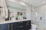 Experience modern luxury in this stunning bathroom featuring a sleek dark vanity with gold hardware and dual sinks.