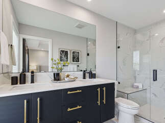 Experience modern luxury in this stunning bathroom featuring a sleek dark vanity with gold hardware and dual sinks.
