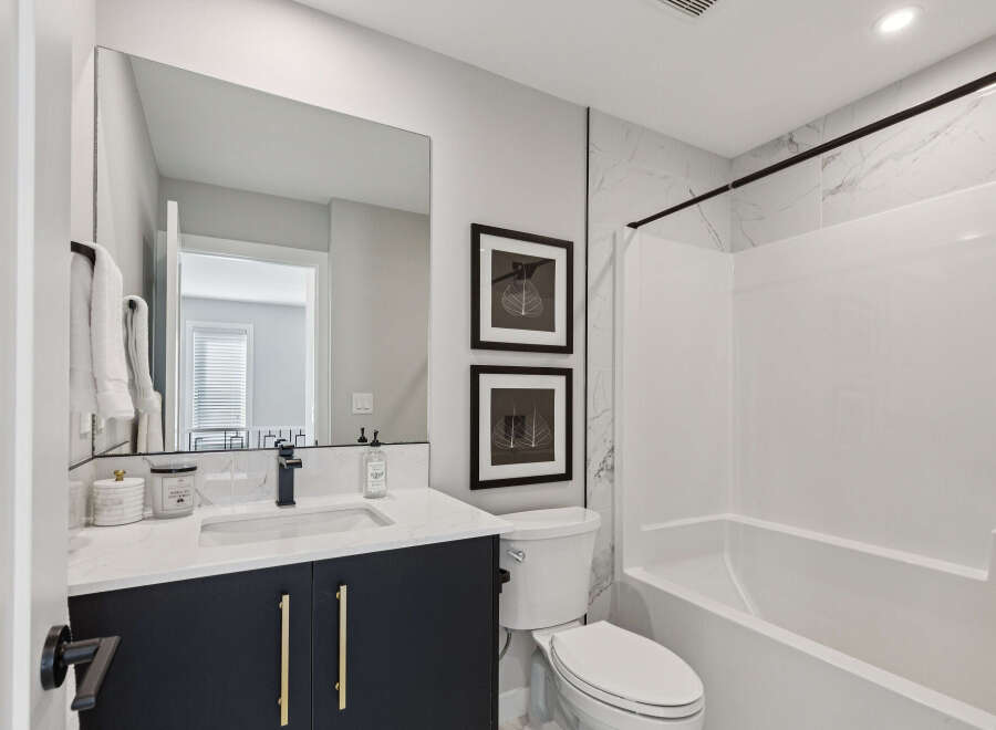 This modern bathroom features a sleek vanity with gold hardware and a quartz countertop, complemented by a large mirror and elegant marble tile accents.