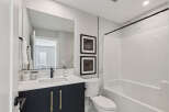 This modern bathroom features a sleek vanity with gold hardware and a quartz countertop, complemented by a large mirror and elegant marble tile accents.