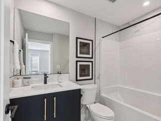 This modern bathroom features a sleek vanity with gold hardware and a quartz countertop, complemented by a large mirror and elegant marble tile accents.