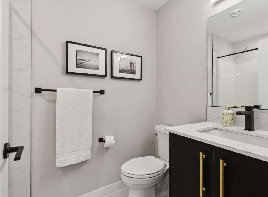 This modern bathroom features a sleek black vanity with gold hardware, complemented by a white quartz countertop and a matte black faucet.