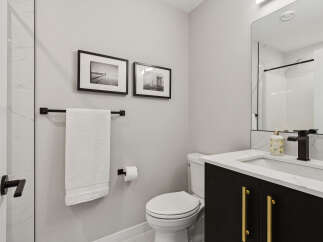 This modern bathroom features a sleek black vanity with gold hardware, complemented by a white quartz countertop and a matte black faucet.