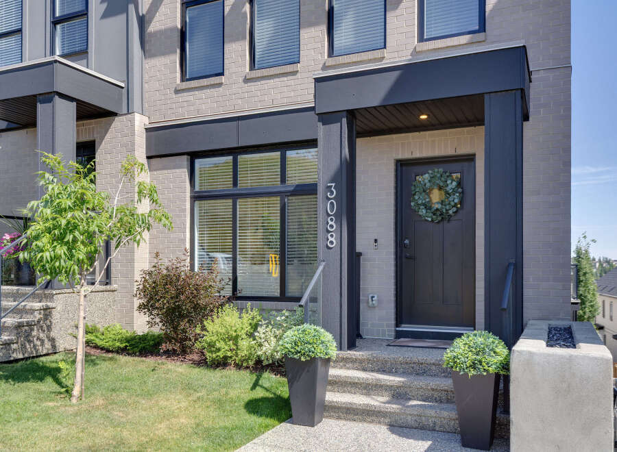 Modern townhouse featuring a sleek dark gray front door adorned with a lush eucalyptus wreath, complemented by a contemporary brick facade and large windows.