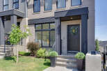 Modern townhouse featuring a sleek dark gray front door adorned with a lush eucalyptus wreath, complemented by a contemporary brick facade and large windows.