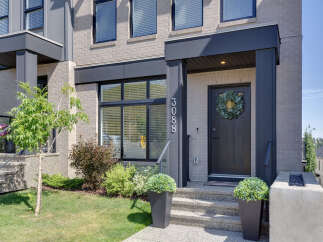 Modern townhouse featuring a sleek dark gray front door adorned with a lush eucalyptus wreath, complemented by a contemporary brick facade and large windows.