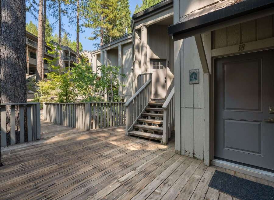 Step onto the charming wooden deck and ascend the stairs to this inviting entrance, nestled amongst mature trees.