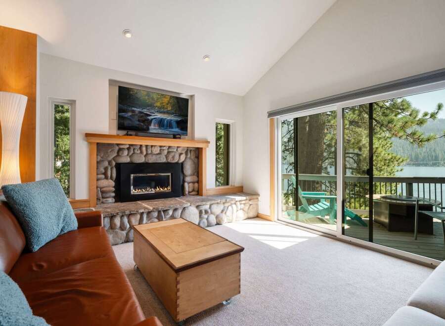 Experience breathtaking lake views from this stunning living room, featuring a cozy stone fireplace and a large sliding glass door that opens to a private deck.