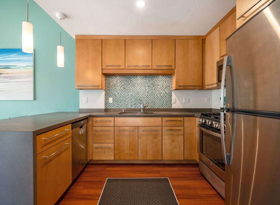 This modern kitchen features sleek, light wood cabinetry complemented by a stylish mosaic tile backsplash.