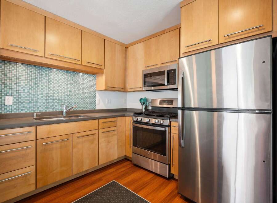 This modern kitchen features sleek, light wood cabinetry complemented by a striking mosaic tile backsplash.