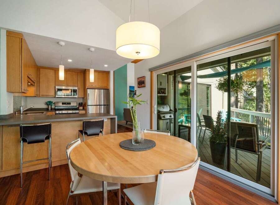 This modern kitchen and dining area features sleek, light wood cabinetry and a convenient breakfast bar with seating.