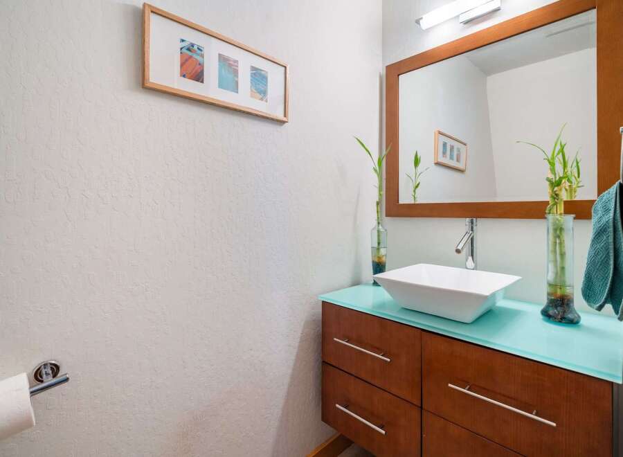 This modern bathroom features a sleek vanity with a vibrant turquoise countertop, topped with a stylish vessel sink and a polished chrome faucet.